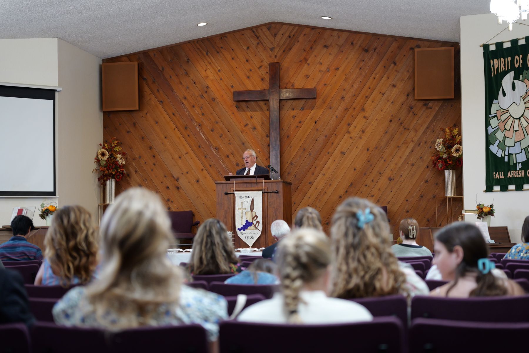 The pastor preaching from the pulpit beneath the cross, with the congregation listening.